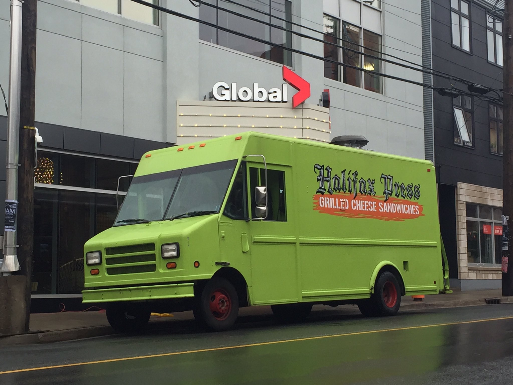 Lime green food truck with Halifax Press full logo along the side, parked in front of Global News.